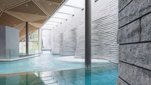 Una piscina interior con diseño moderno, que cuenta con un amplio espacio abierto, techo alto y una serie de paredes de piedra.