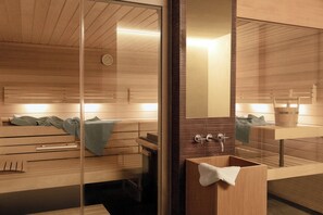 A modern bathroom with wooden paneling, a glass shower enclosure, and a wooden vanity with a towel hanging on it. - Tschuggen Grand Hotel (Arosa)