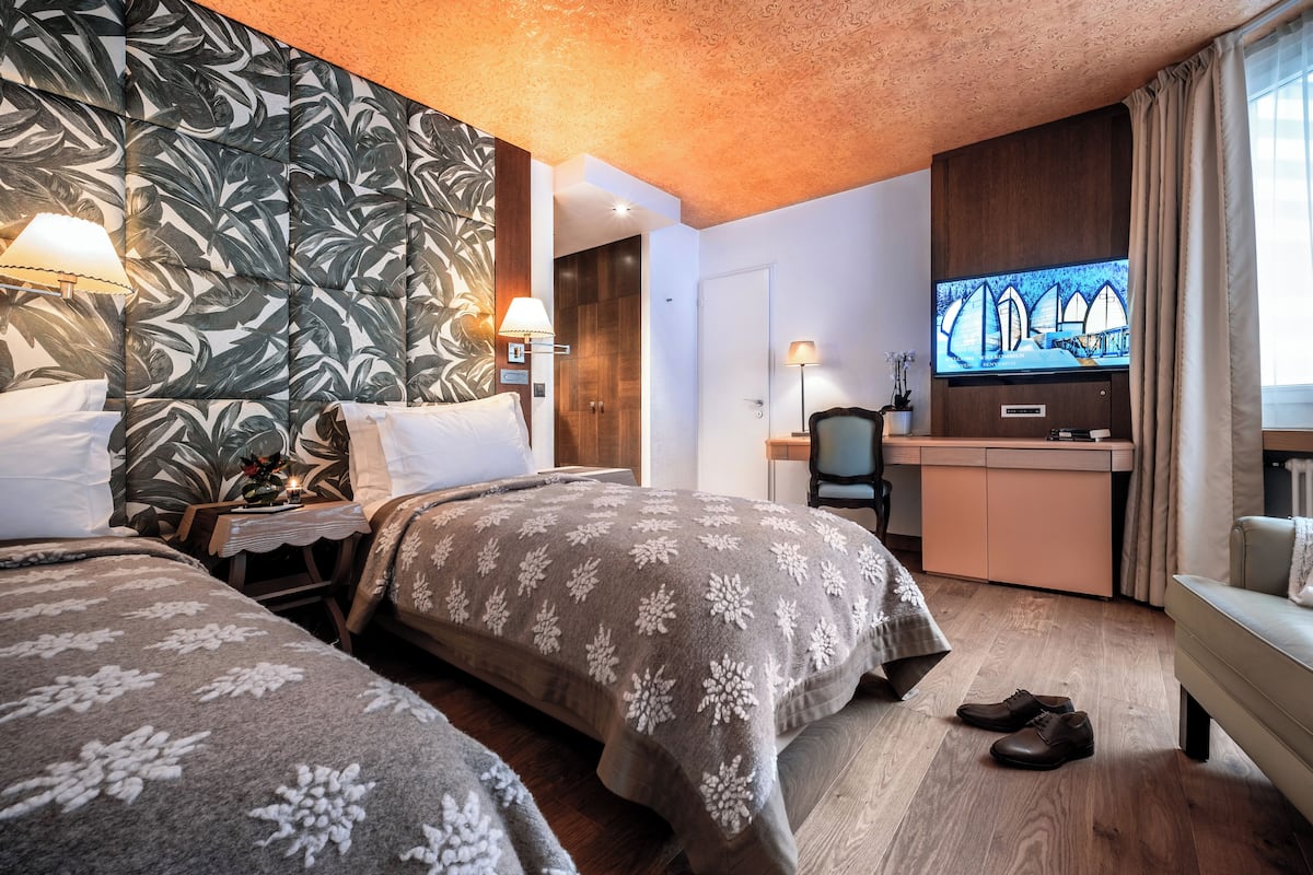 A hotel room with two beds, a desk, a television, and a chair.