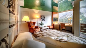 A bedroom with a large bed, a desk, a chair, and a window with a mountain view.