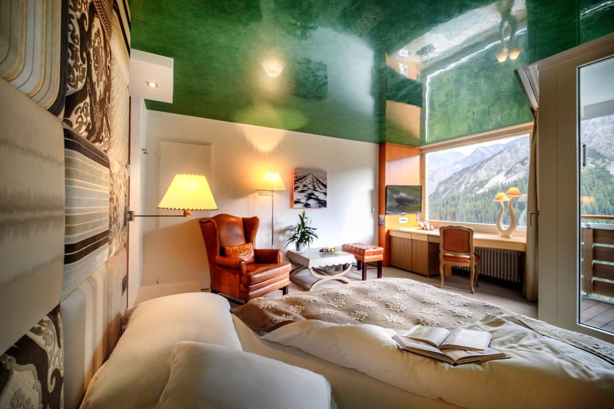 A bedroom with a large bed, a desk, a chair, and a window with a mountain view.