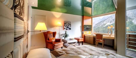 Un dormitorio con una cama grande, un escritorio, una silla y ventana con vista a la montaña.