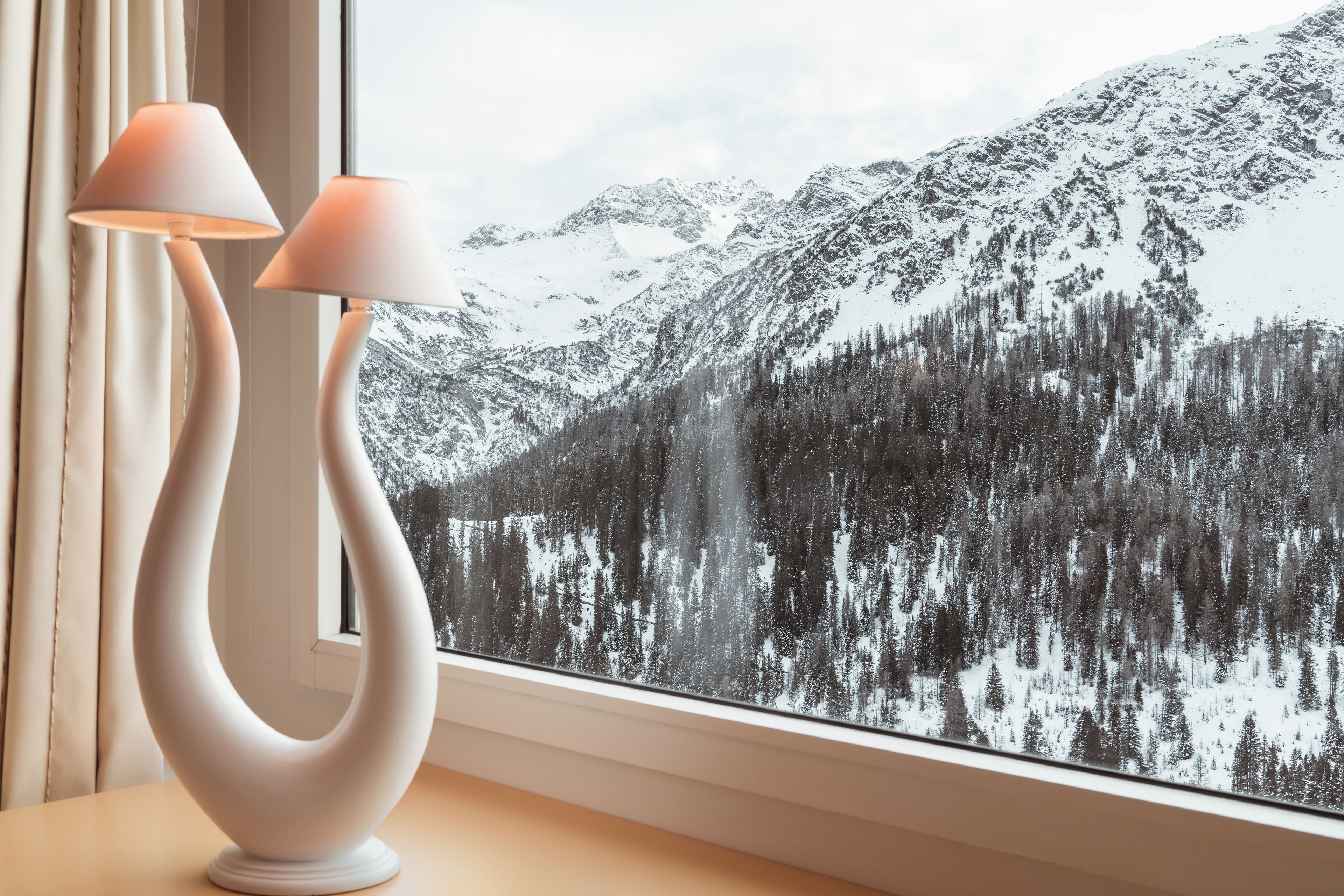 Eine moderne Lampe mit originellem Design steht auf einem Tisch neben einem Fenster mit Blick auf einen verschneiten Berg.
