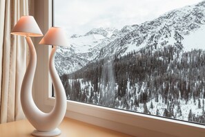 Una lámpara moderna con un diseño único sobre una mesa junto a una ventana que ofrece vistas a una montaña nevada.