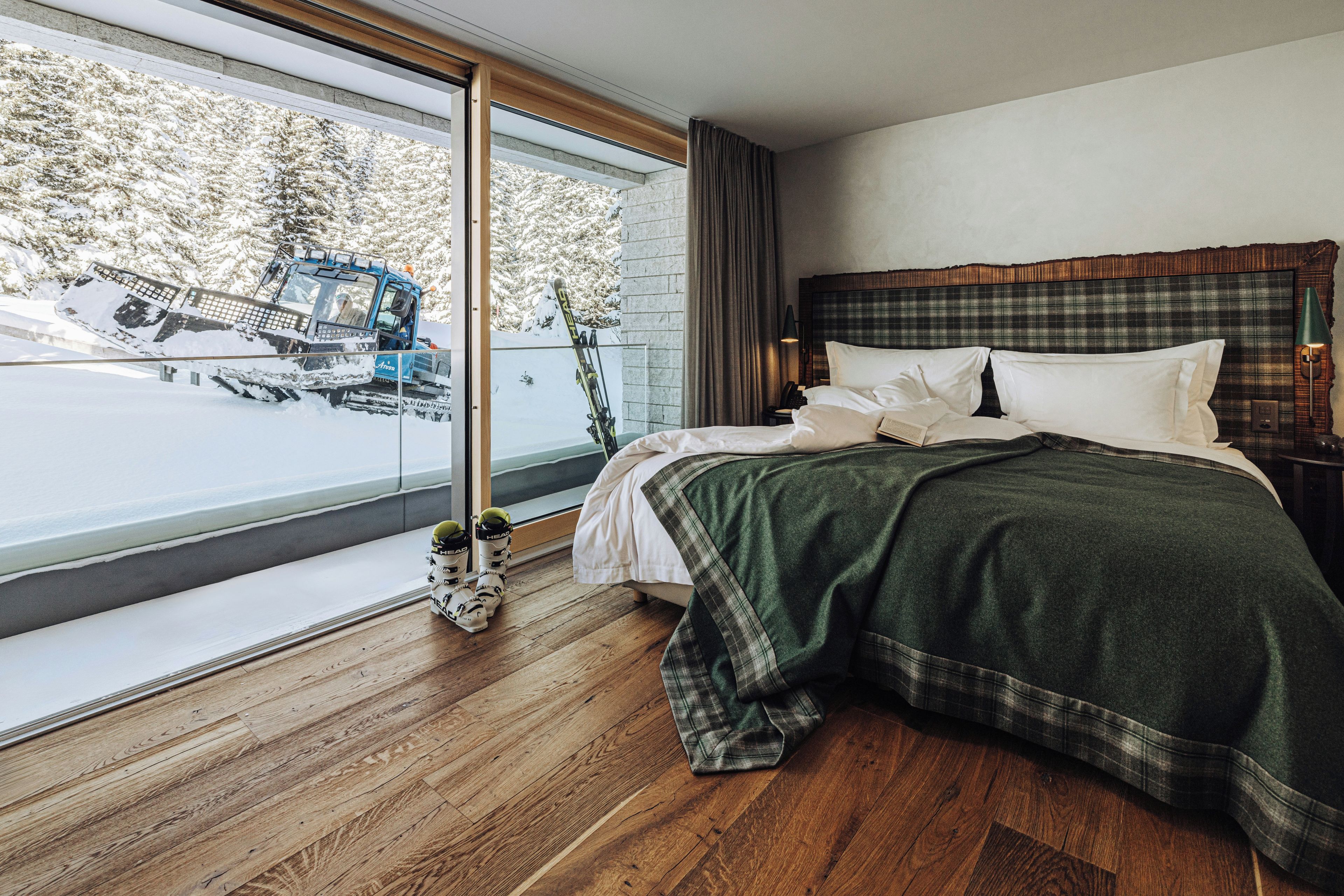 A hotel room with a large window, a bed with a plaid headboard, and a view of a snow-covered landscape.
