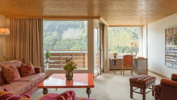 A spacious room with a sofa, a small table with a vase, a desk with a chair, and a view of a forested area.