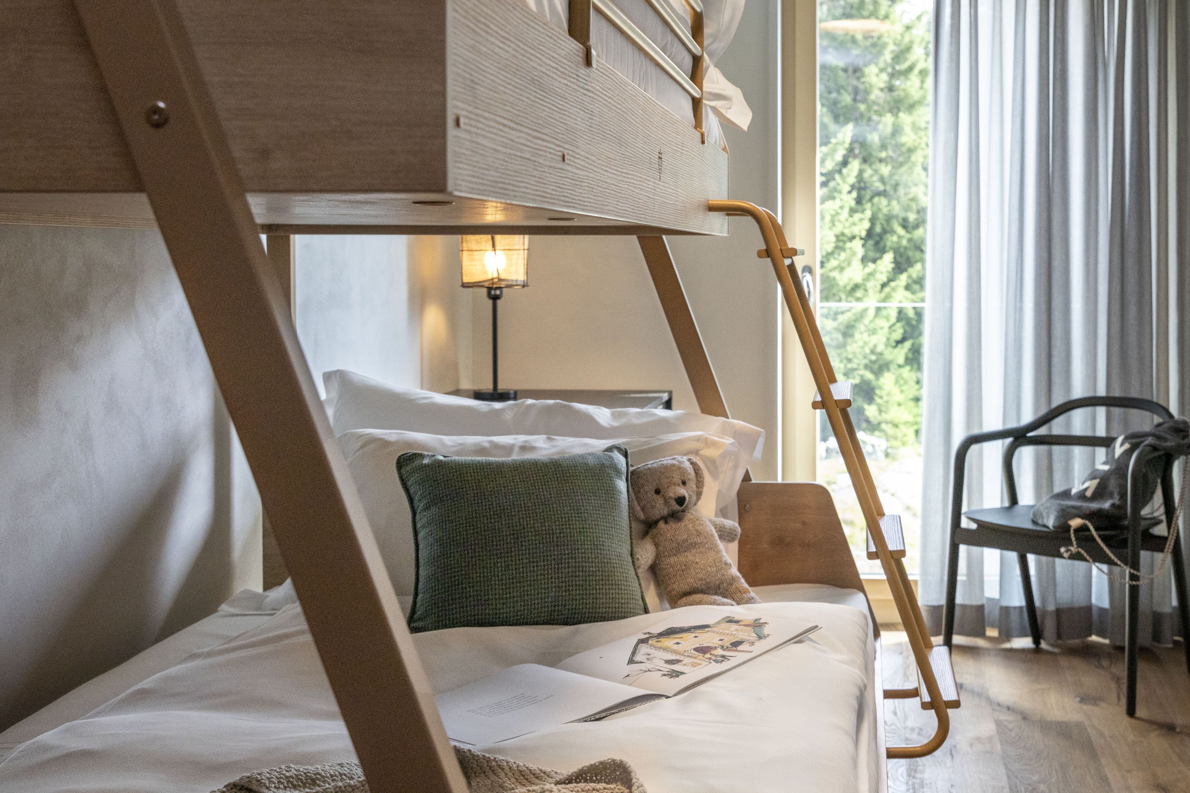 Una cama litera con escalera, un almohadón verde, un osito de peluche y un libro en la cama.