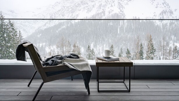 Un balcón con una silla y una mesita, con vistas a un paisaje montañoso nevado.