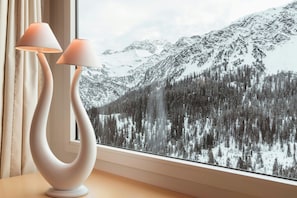 A modern lamp with a unique design on a table by a window with a view of snow-covered mountains.