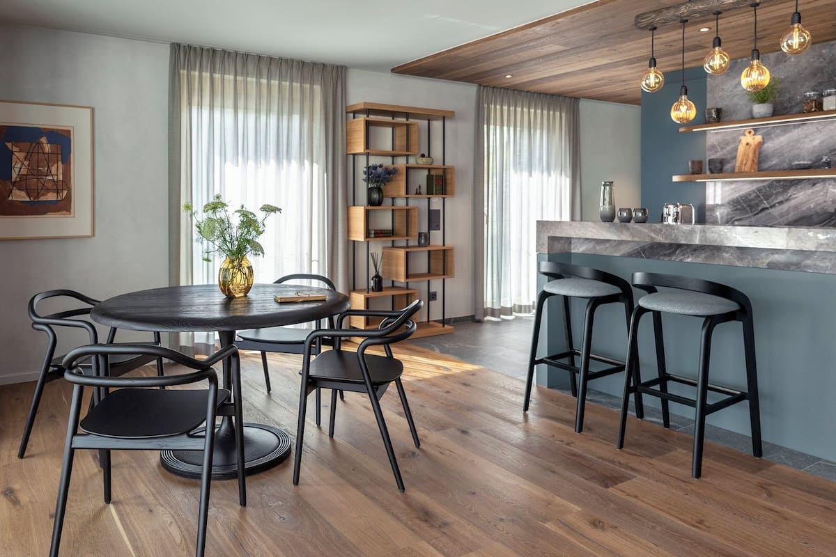 A modern kitchen with a wooden island, bar stools, and a built-in bookshelf.