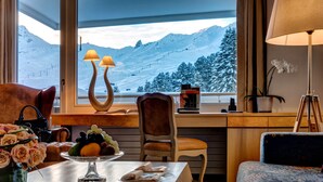 Una habitación acogedora con vistas a montañas nevadas, una mesa de comedor con frutas y flores, y una zona de estar confortable.
