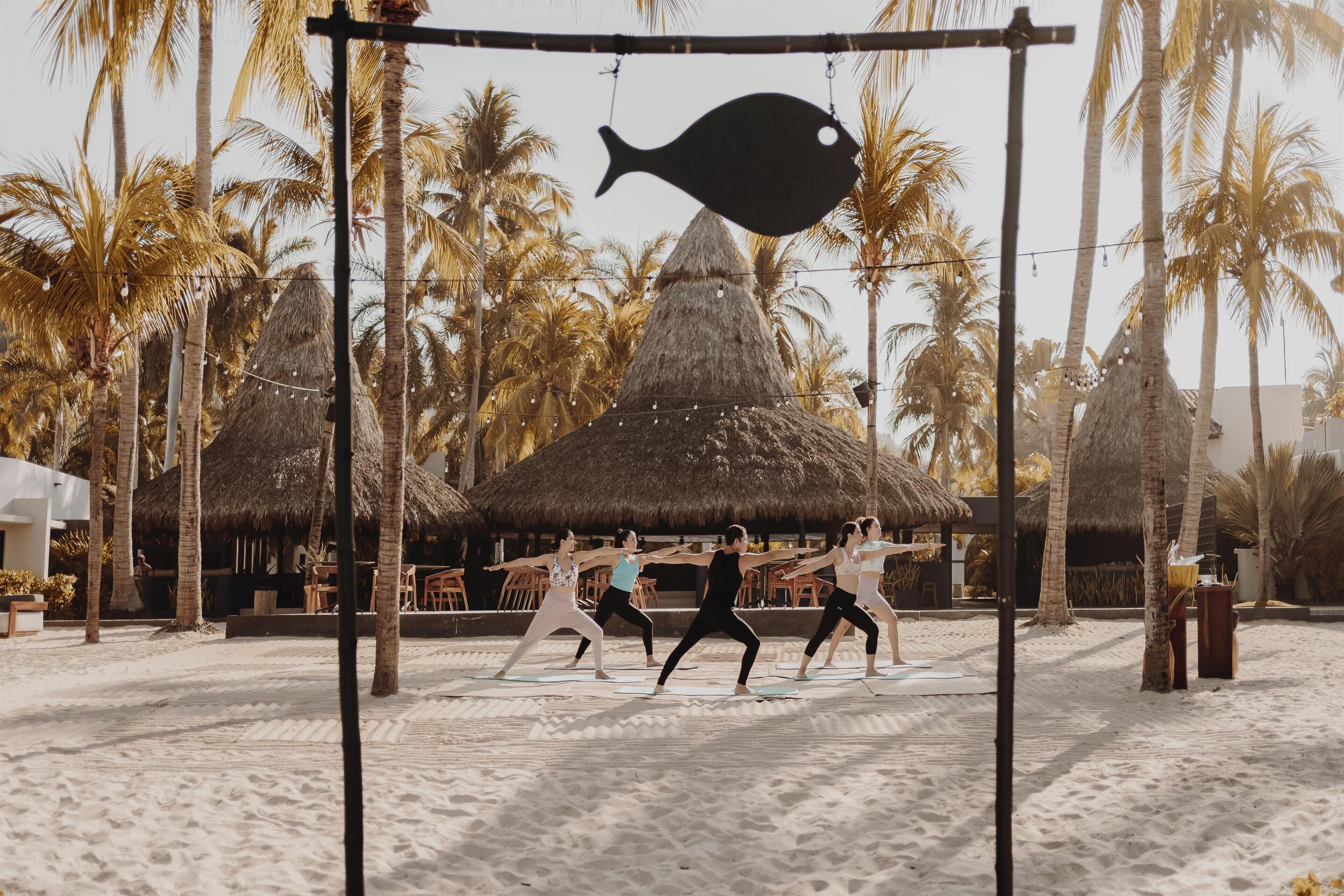 A beach with palm trees, a thatched-roof hut, and people exercising.