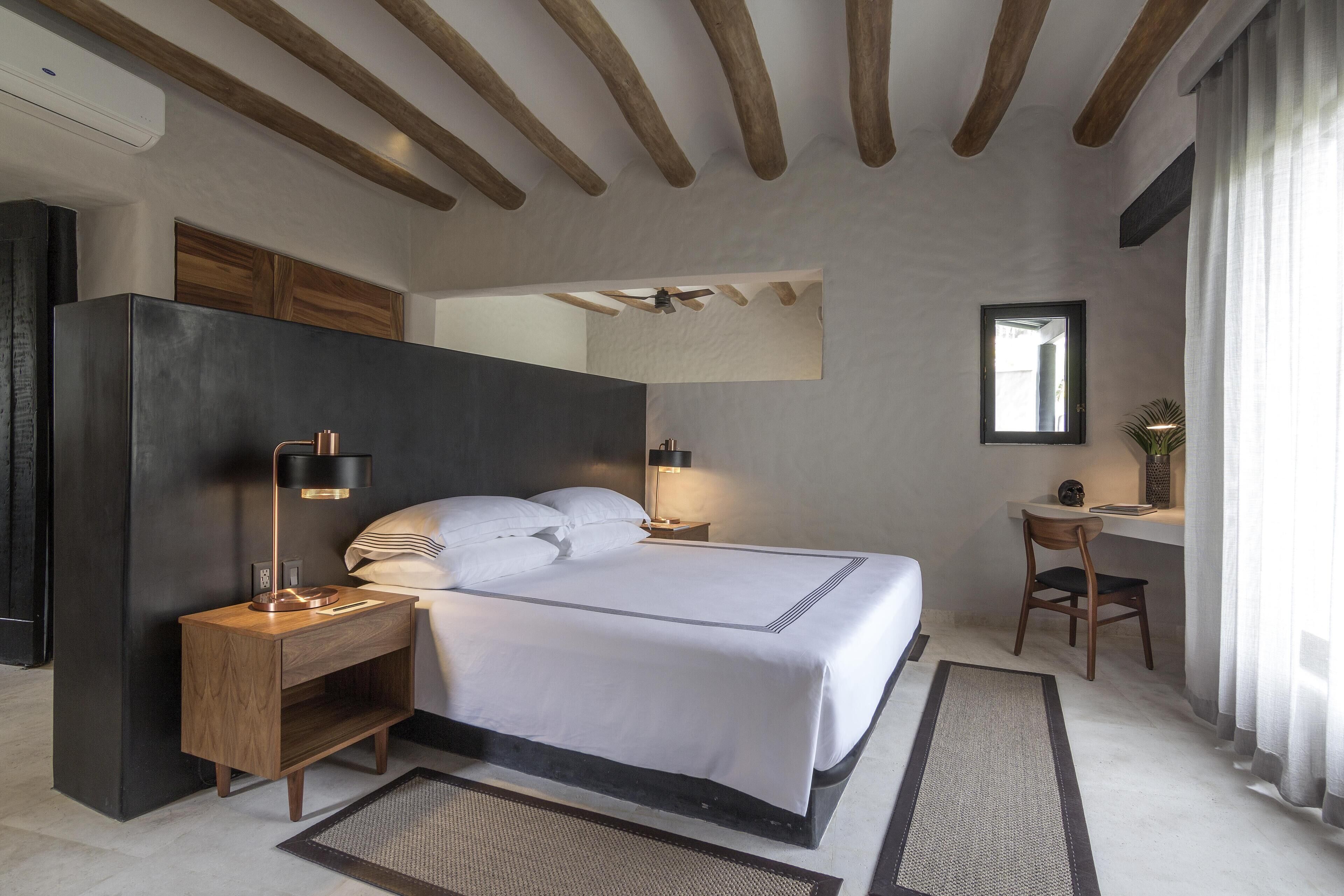 A modern hotel room with a bed, bedside tables, a desk, and a chair.