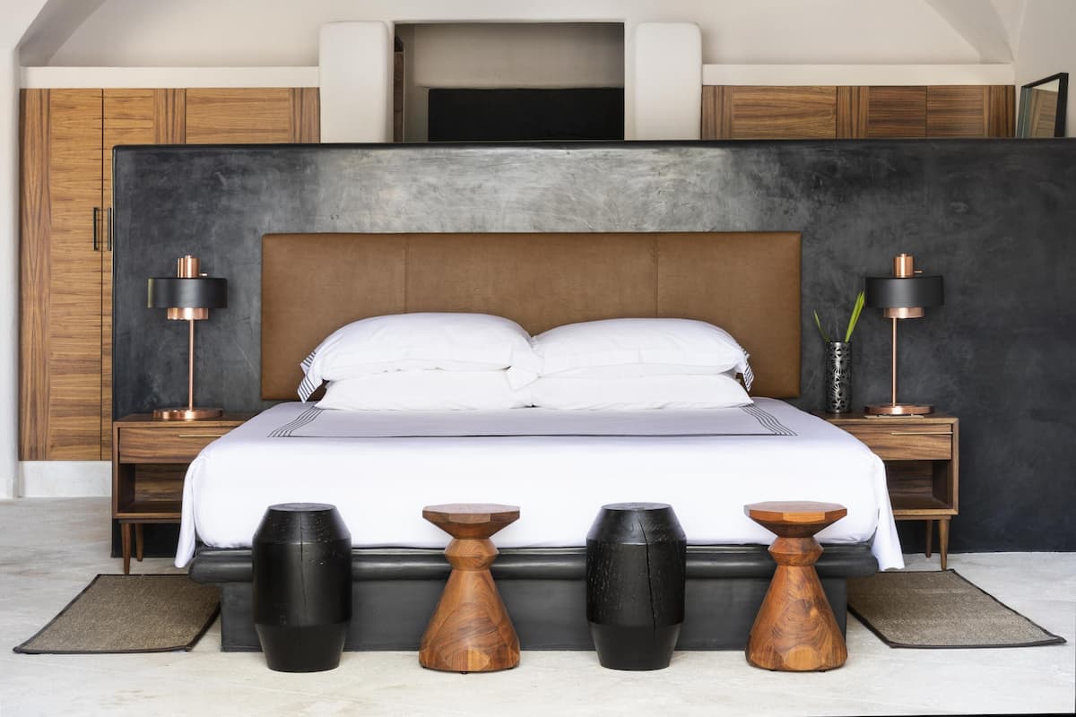 A modern bedroom with a large bed, wooden headboard, two bedside tables with lamps, and a dark accent wall.