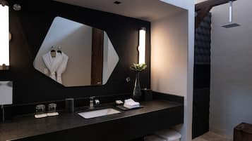 A modern bathroom with a large mirror, dark countertop, and a shower area.
