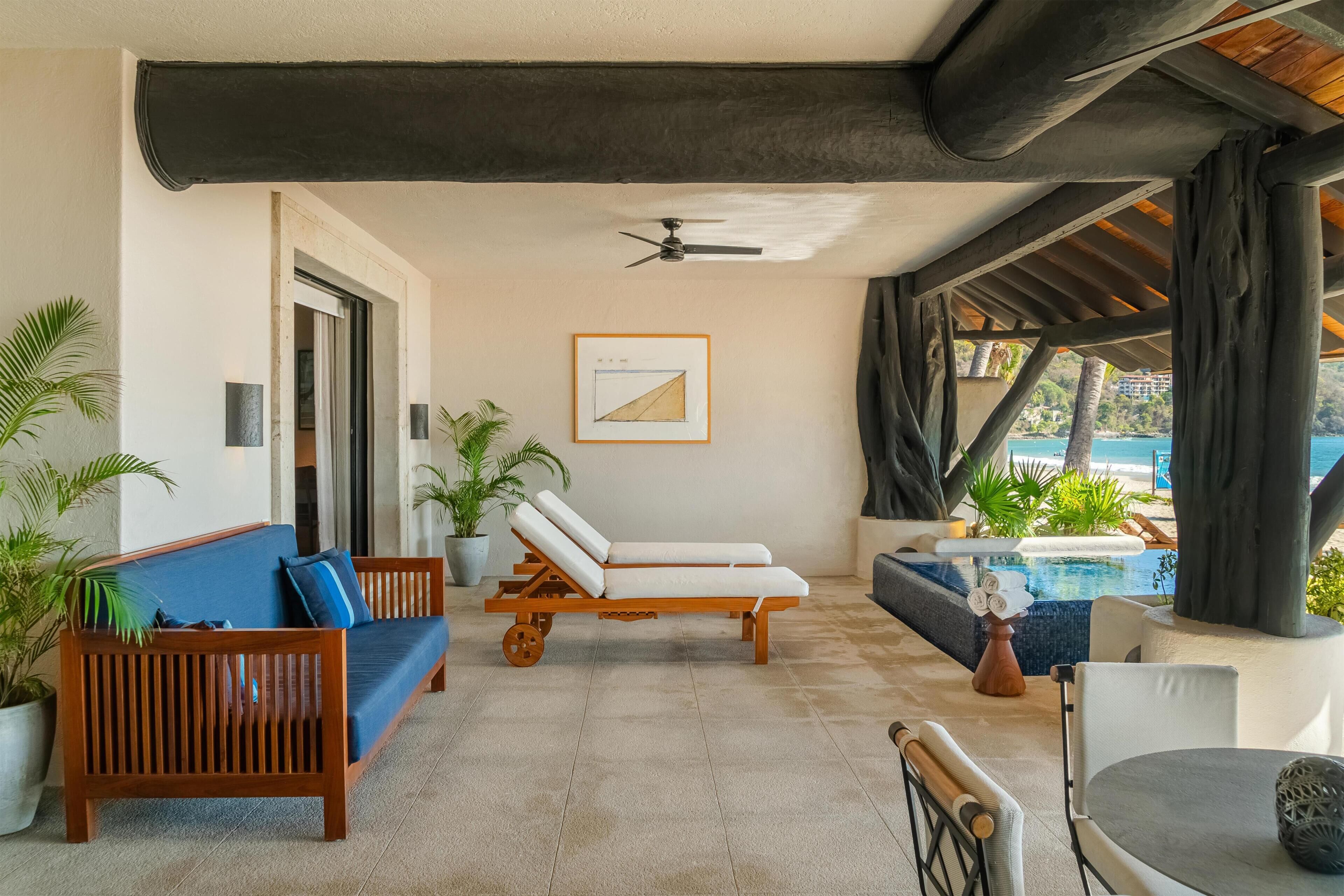 A sunlit lounge area with a wooden sofa, a lounge chair, and a pool view.