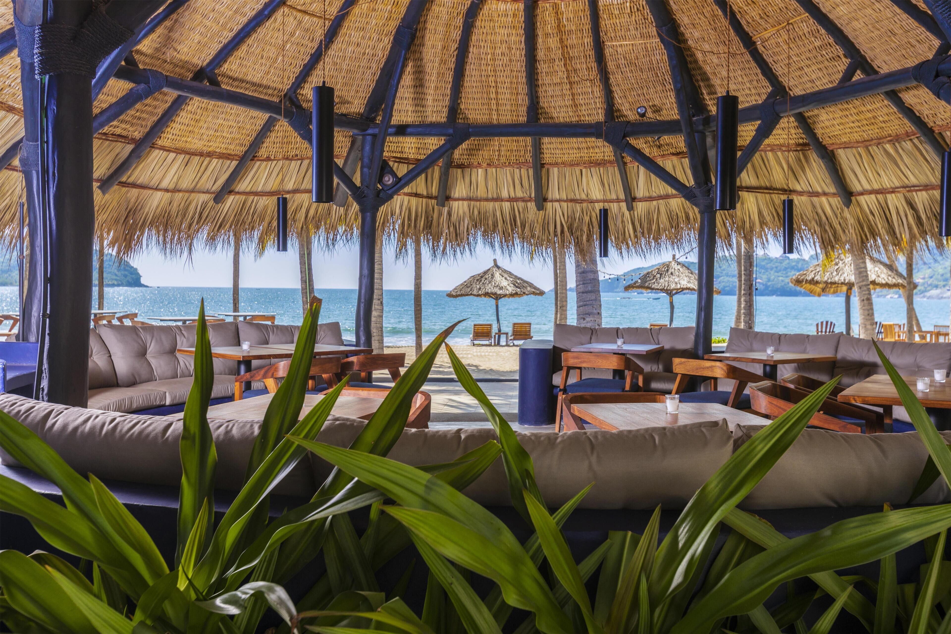 An outdoor seating area with thatched umbrellas, cushioned seating, and a view of the sea.
