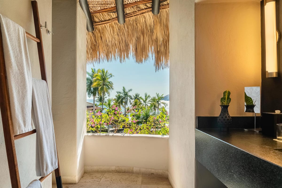 A bathroom with a view of palm trees and flowers, a towel rack, a sink, and a potted plant.