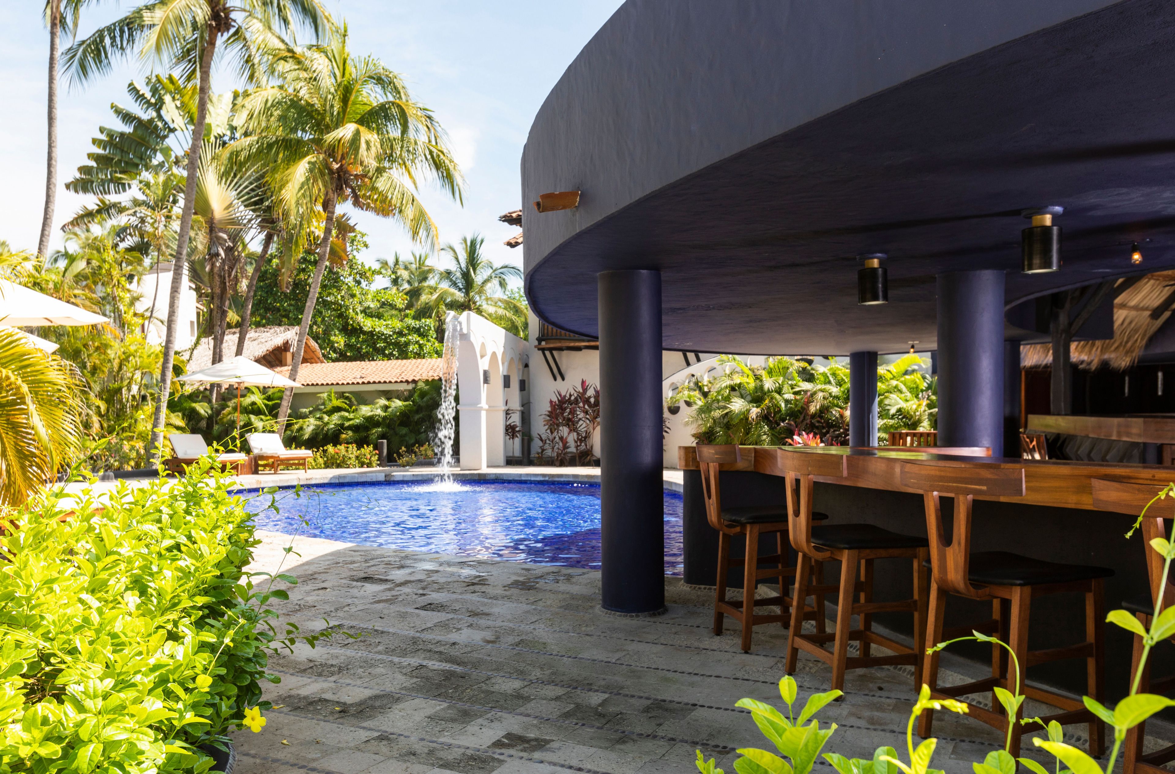 A pool area with a bar and seating, surrounded by palm trees and greenery.