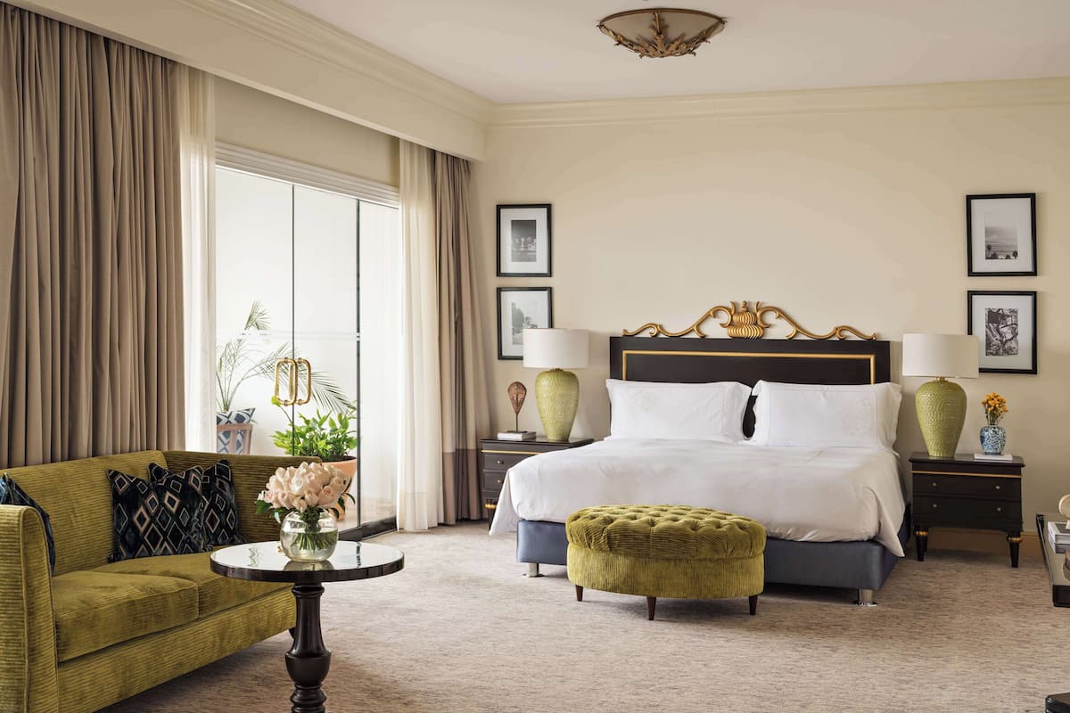 A hotel room with a large bed, a sofa, a small table, and a potted plant.