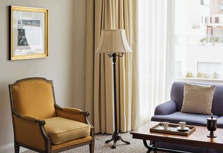A hotel room with a bed, a sofa, a chair, a floor lamp, a table with a tray, and a framed picture on the wall.