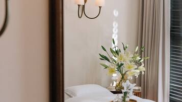 Habitación de hotel con cama, mesita de noche, espejo, lámpara de pared y ventana con cortinas.