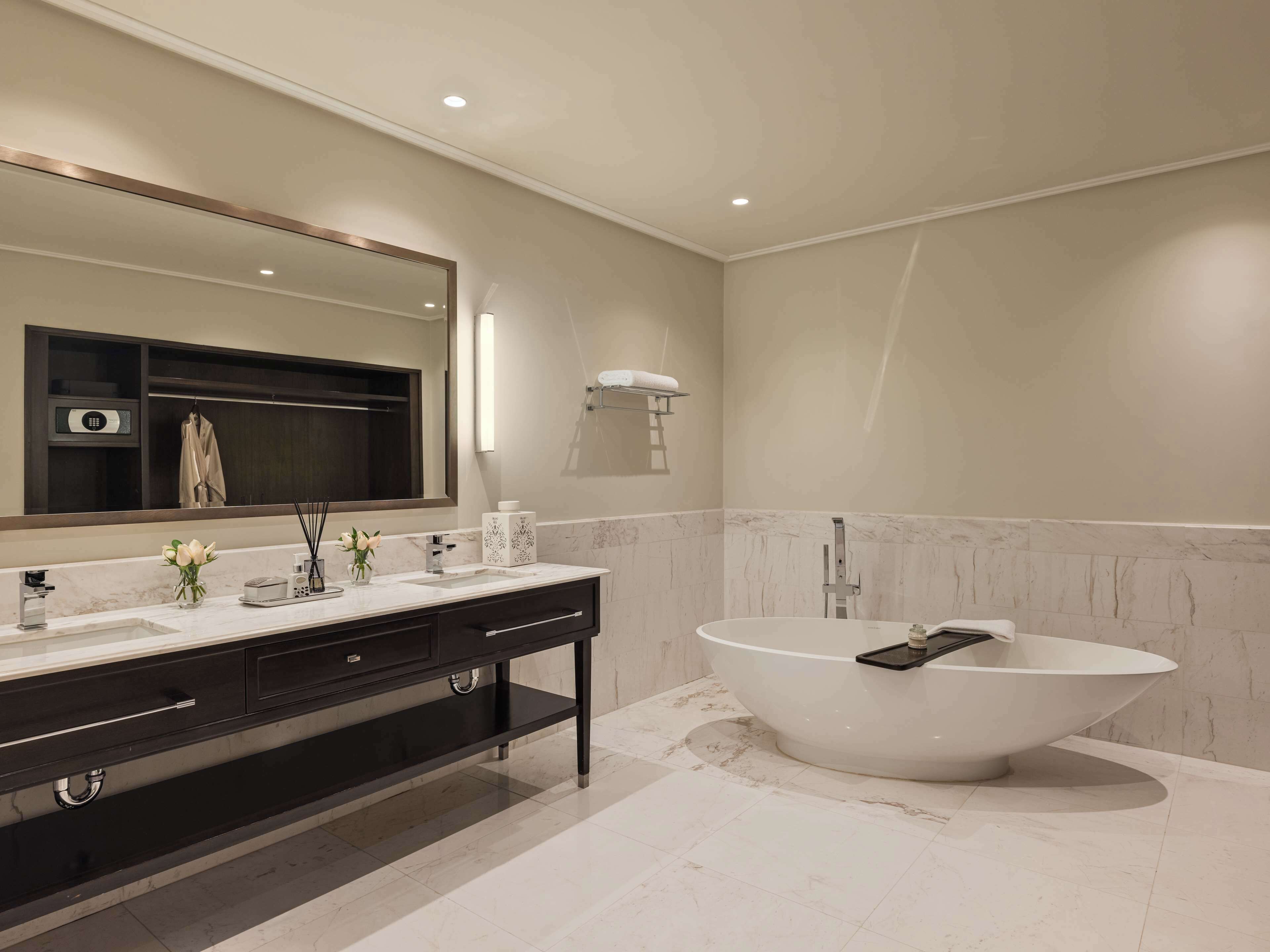 A modern bathroom with a large freestanding bathtub, a dark vanity with a mirror, and a towel rack.