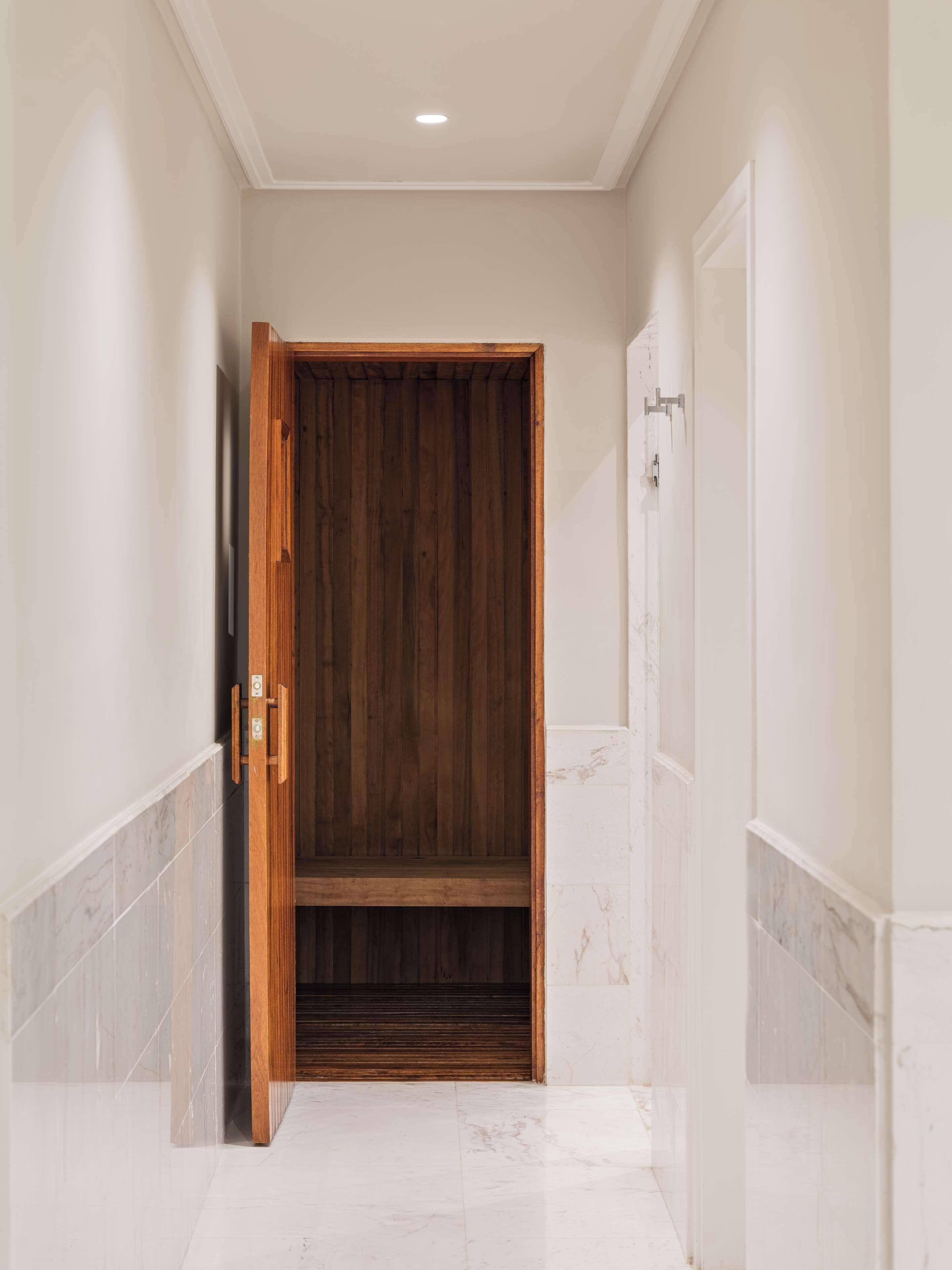 Un pasillo con puerta de madera, suelo de mármol y una lámpara en el techo.