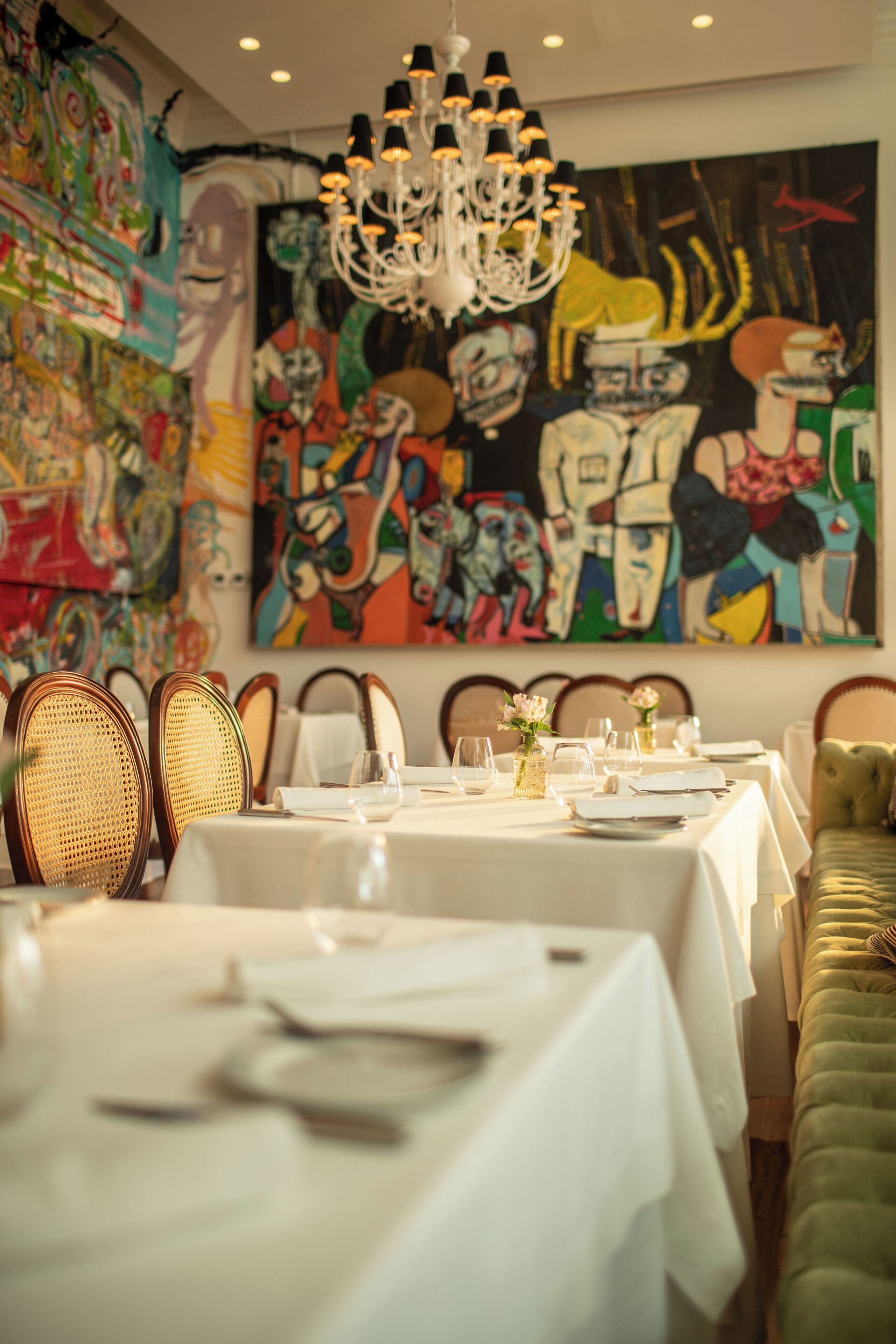 Un comedor con mesas dispuestas para el servicio, una araña y arte abstracto en la pared.