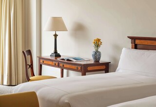 A hotel room with a bed, a desk with a lamp, a chair, and a vase with flowers.
