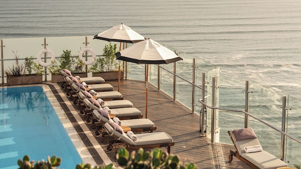 A poolside area with lounge chairs and umbrellas overlooking the ocean.
