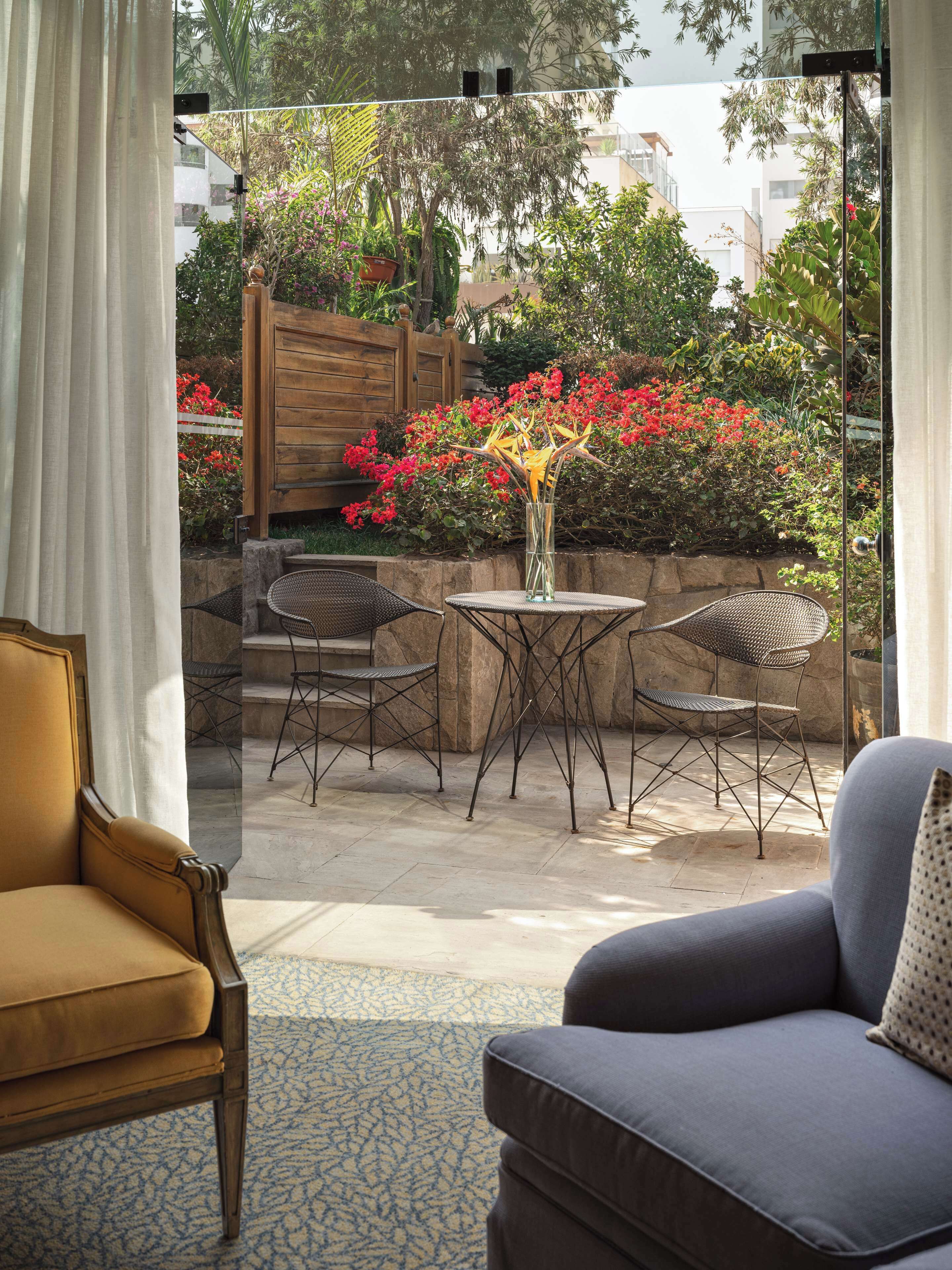 A room with a view of a garden, a dining table with chairs, and a sofa.