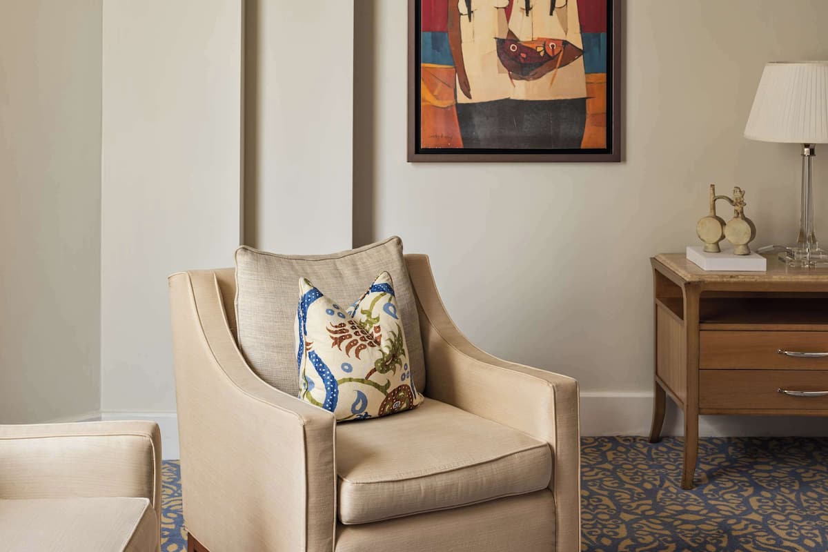 A modern living room with a beige armchair, a glass coffee table, and a framed abstract painting on the wall.