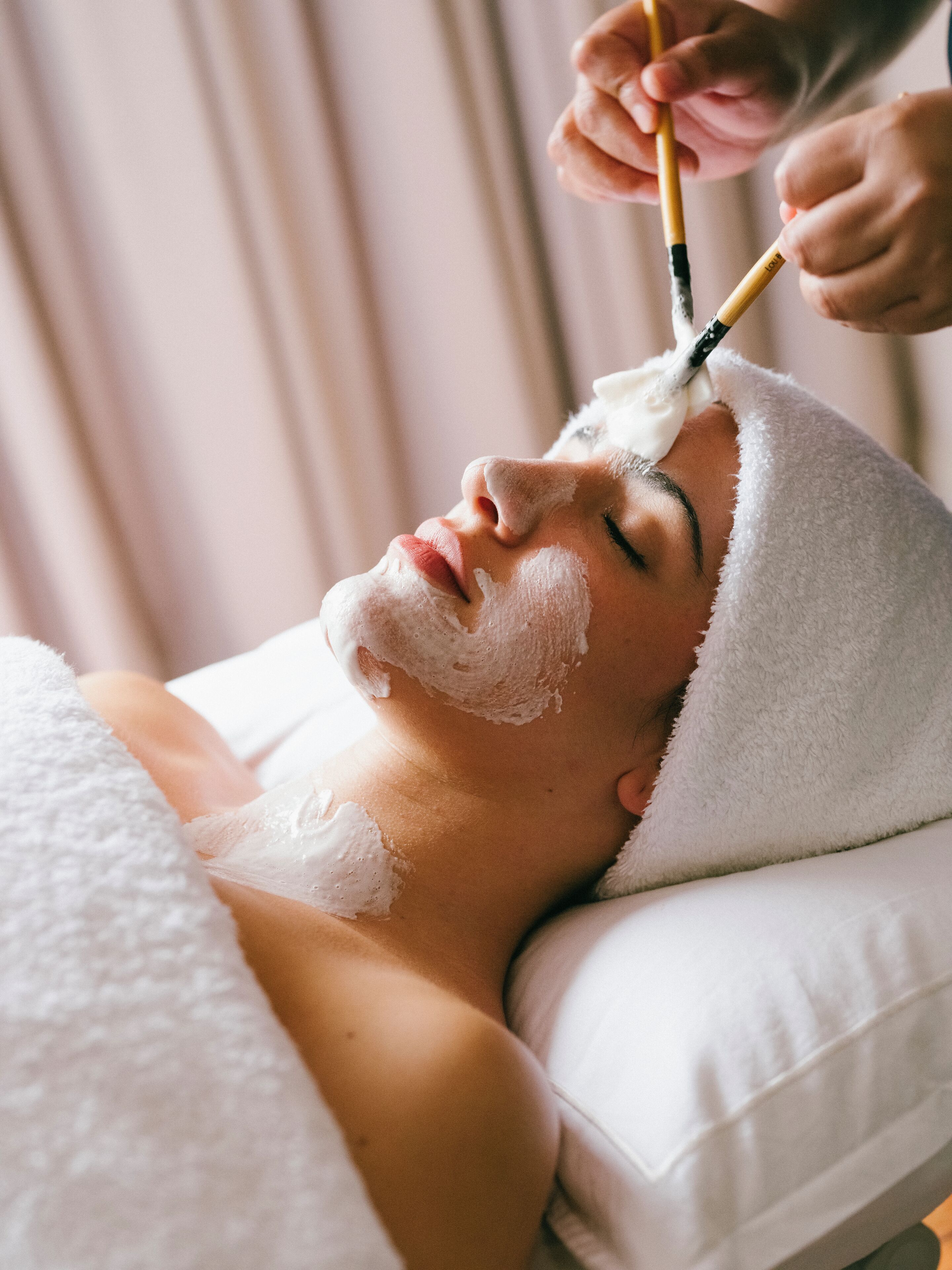 A person lying down with a towel wrapped around their head, receiving a facial treatment.
