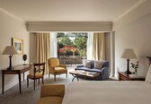 A hotel room with a bed, a sofa, a chair, a small table, a desk, and a view of the outdoors.