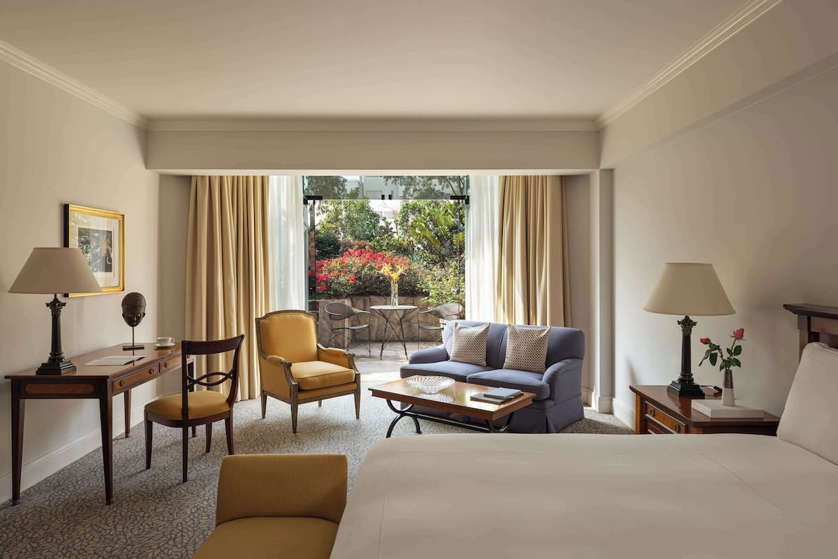 A hotel room with a bed, a sofa, a chair, a desk, and a small balcony with a table and chairs.