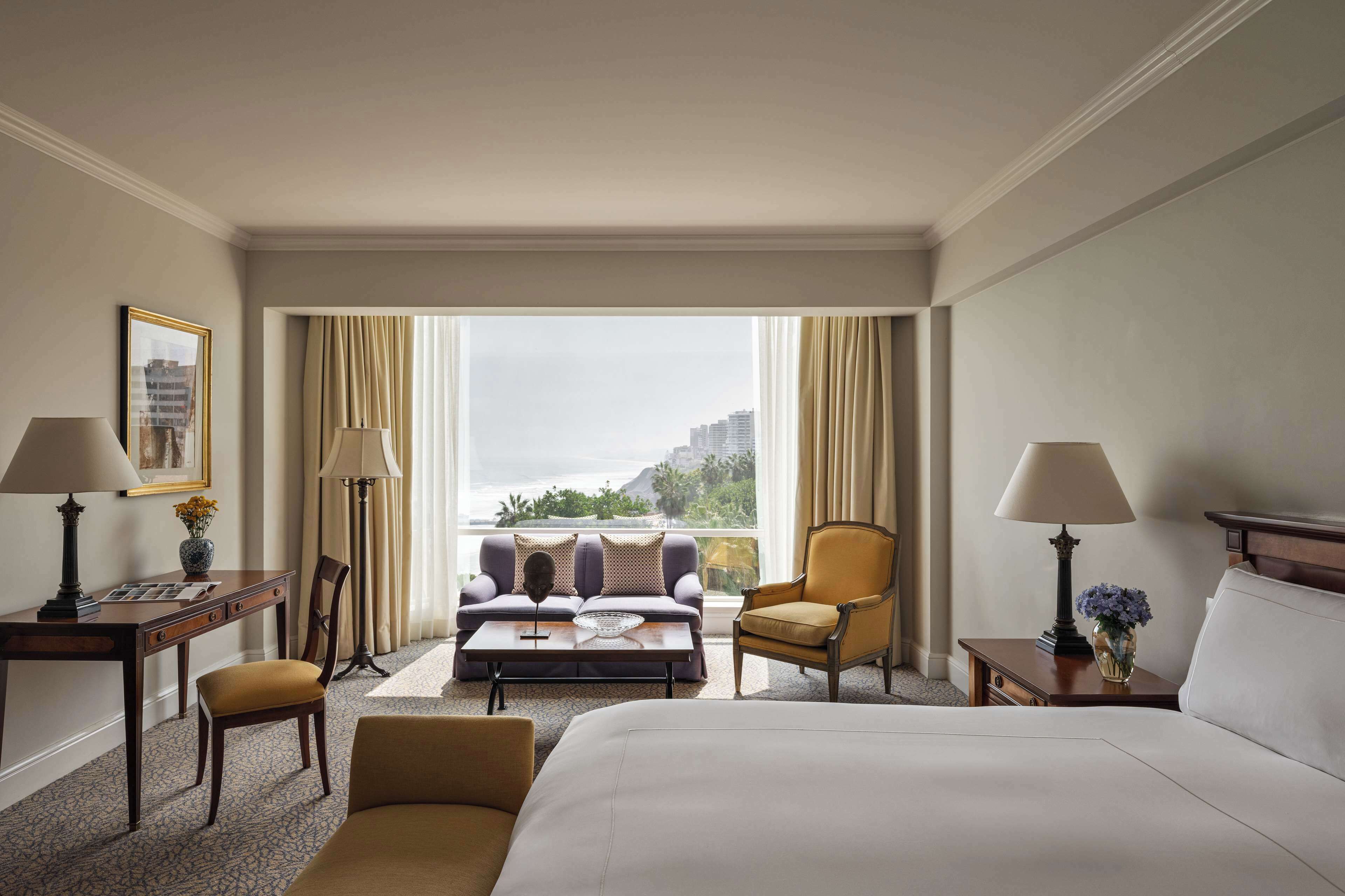 Une chambre d’hôtel avec un lit, un canapé, une chaise, un bureau et une vue sur la ville.