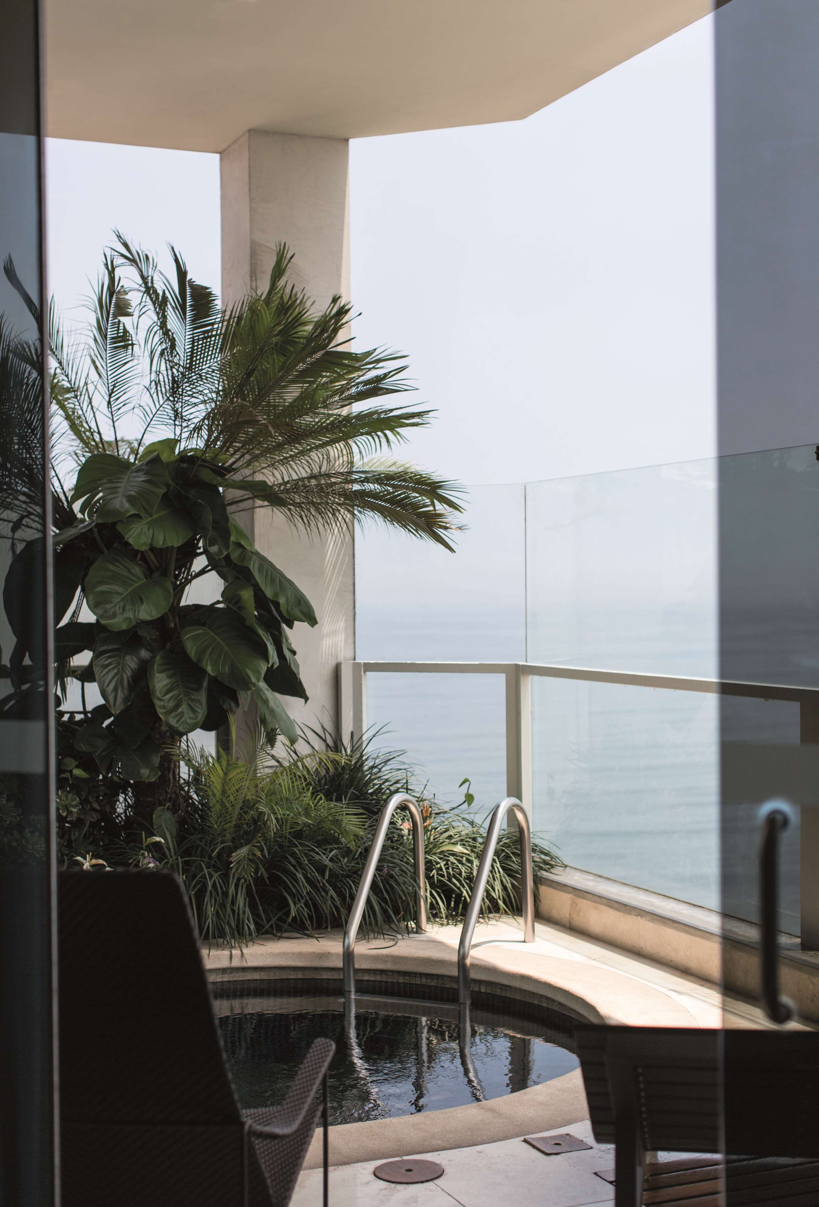 Zona de piscina con vista al océano, rodeada de follaje y arquitectura moderna.