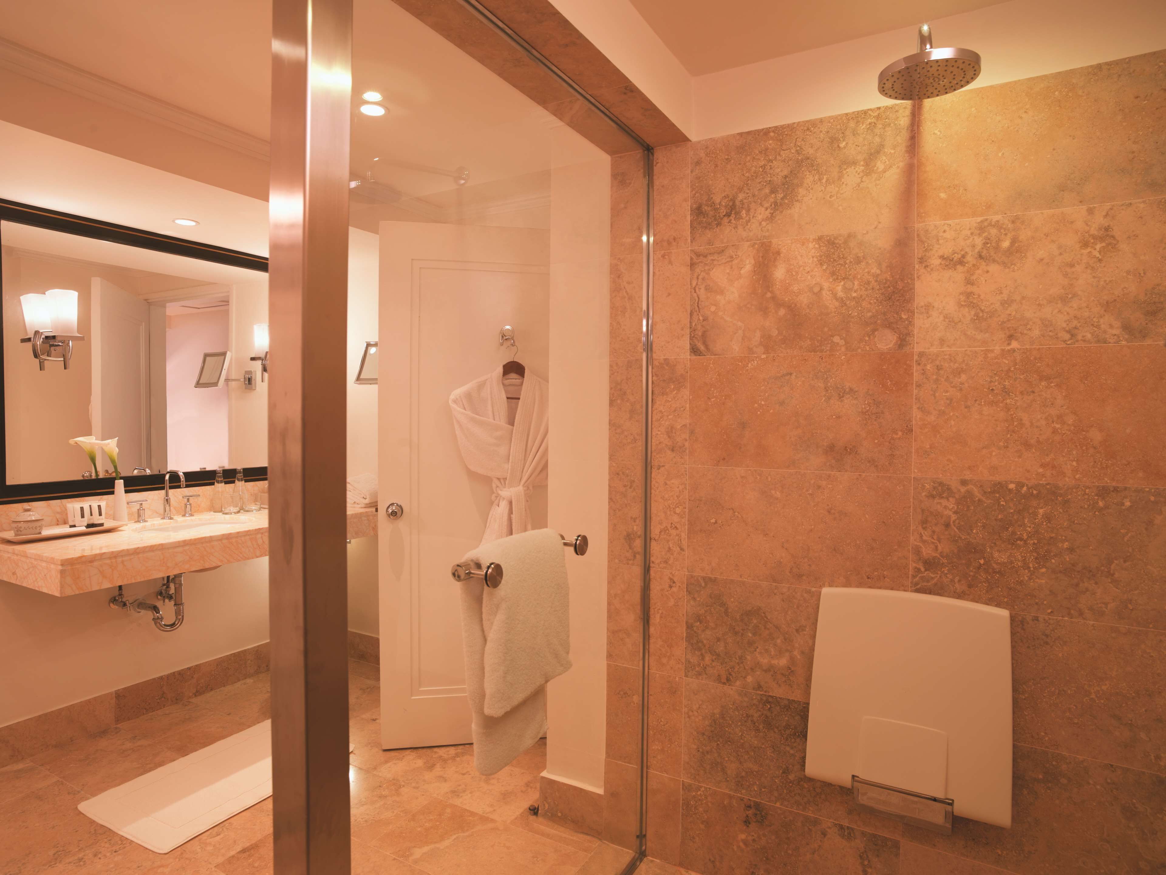 Un baño moderno con cabina de ducha de vidrio, lavamanos de mármol y toallero blanco.