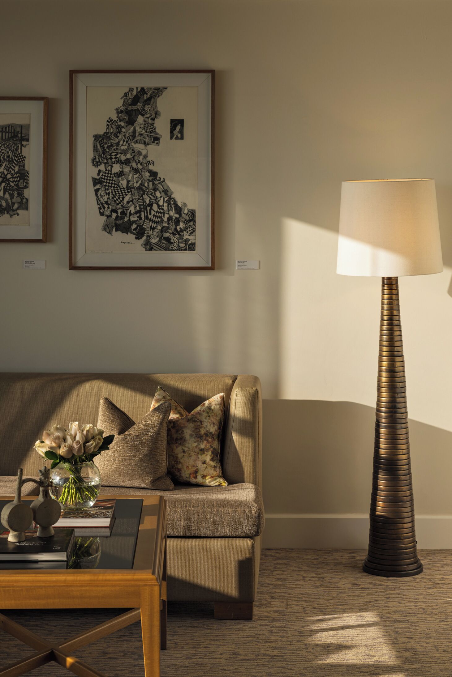 A living room with a sofa, a coffee table with a vase of flowers, a lamp, and two framed artworks on the wall.
