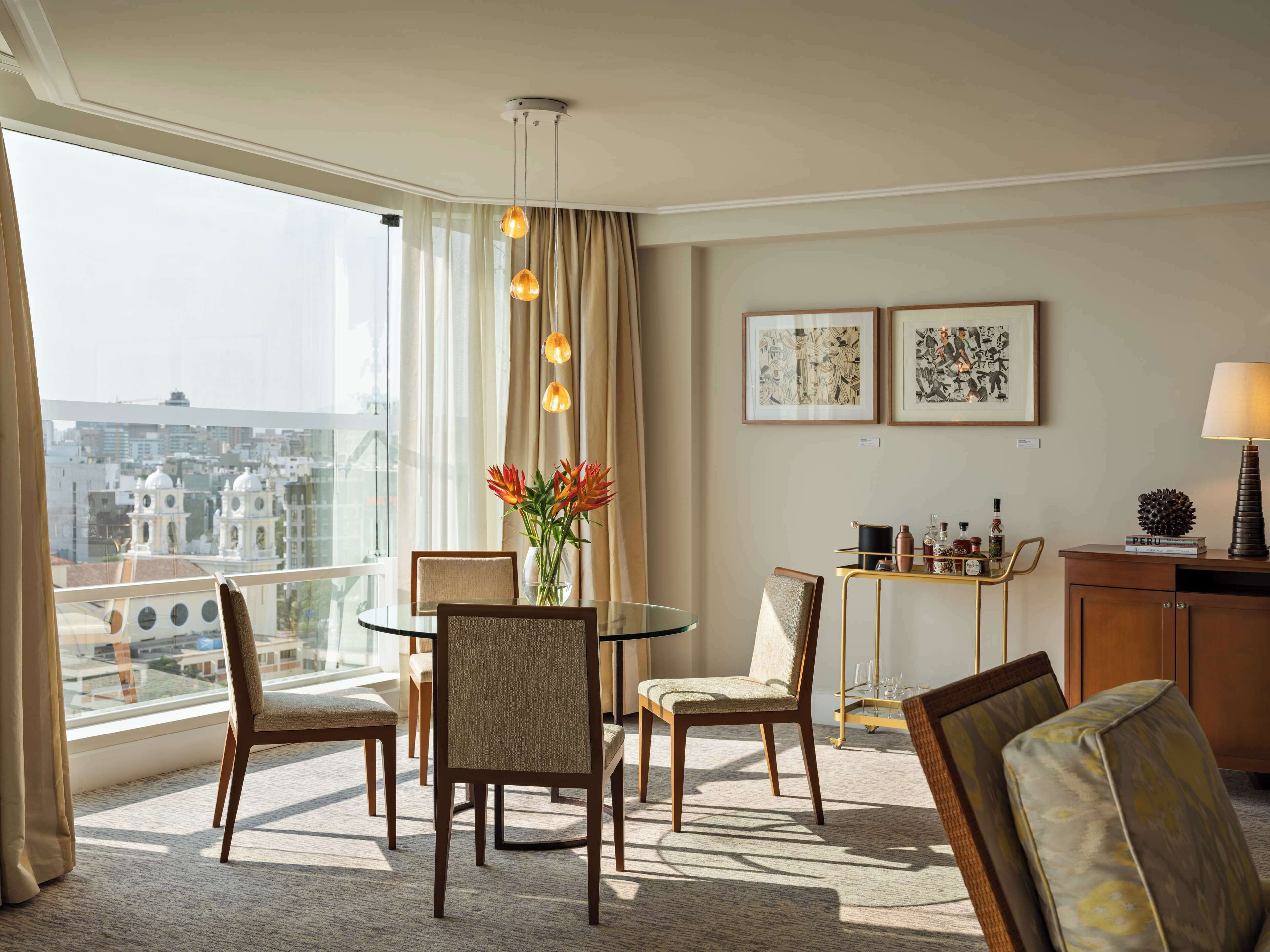Hotelkamer met een eettafel, stoelen, een vaas met bloemen, een kast en lijstwerken aan de muur.