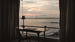 A room with a view of the sea, a table with a lamp, and a chair.