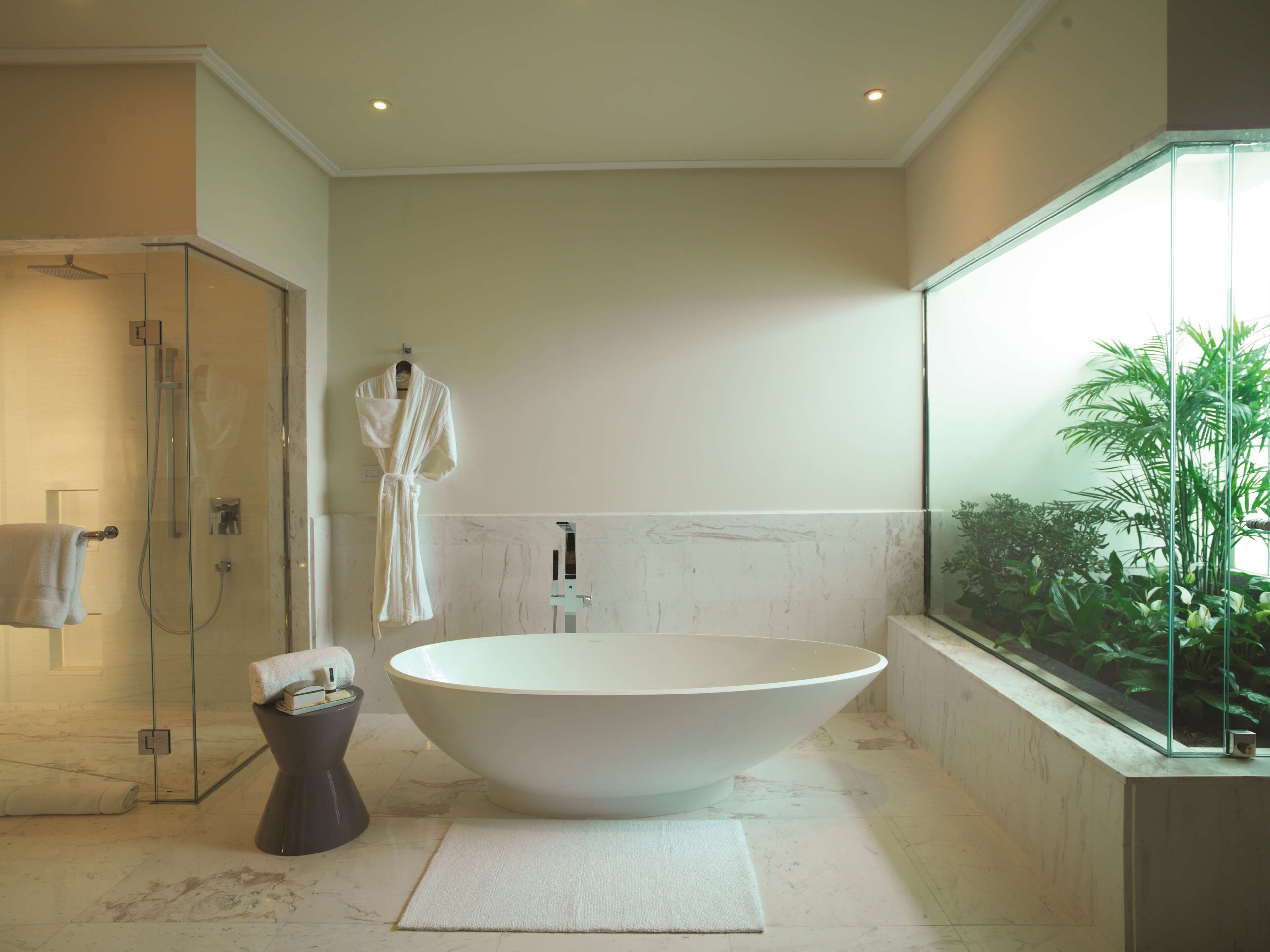 Un baño moderno con una bañera independiente, cabina de ducha de vidrio y un amplio ventanal con plantas.