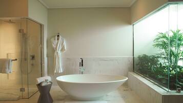 Un baño moderno con una bañera independiente, cabina de ducha de vidrio y un amplio ventanal con plantas.