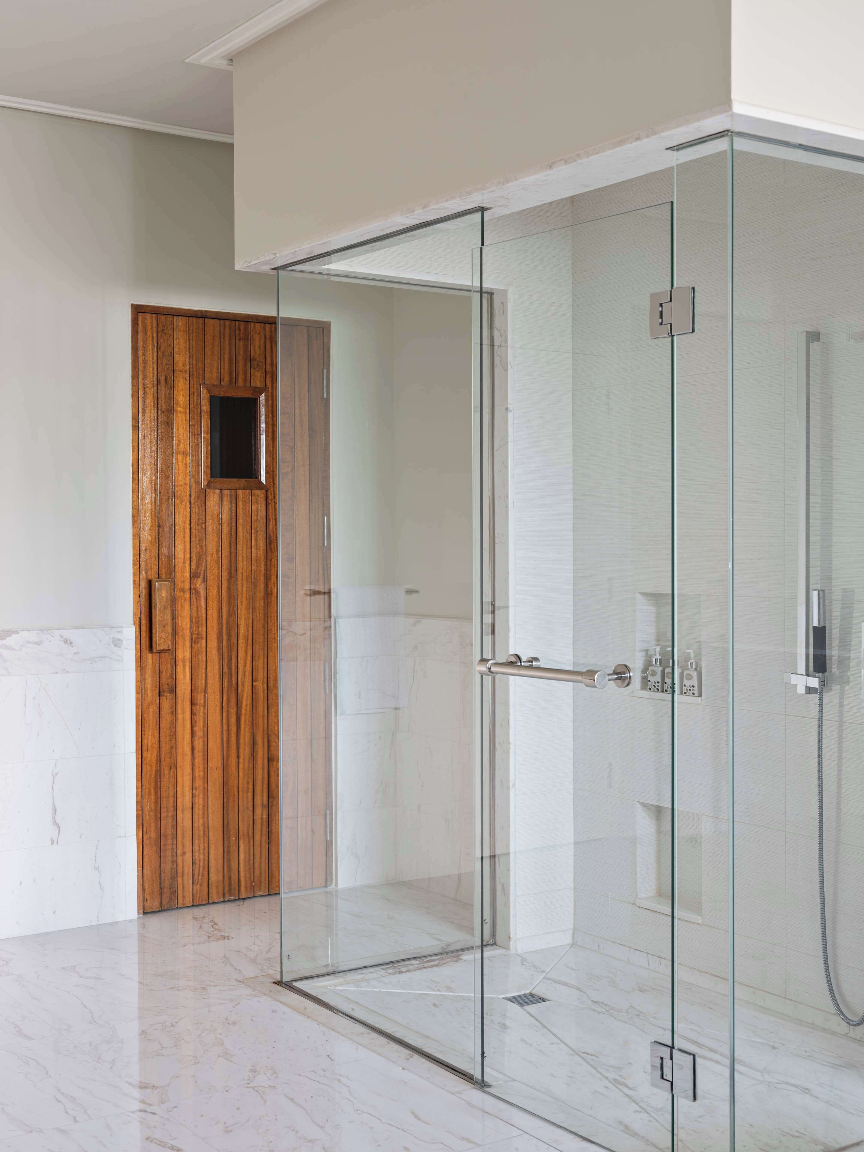 Un baño moderno con ducha de vidrio, puerta de madera y suelo de mármol.