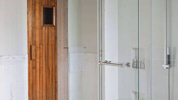 Un baño moderno con ducha de vidrio, puerta de madera y suelo de mármol.