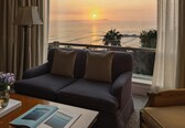 A hotel room with a large window, a sofa, a lamp, and a table with a book.