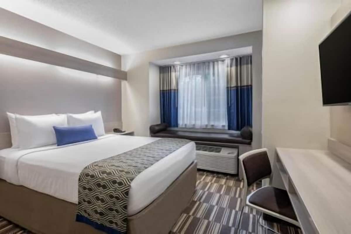 A hotel room with a bed, a desk, a chair, a TV, and a window with curtains.