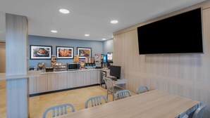 A modern dining area with a long table and chairs, a counter with food displays, and a mounted television. - Microtel Inn & Suites by Wyndham Atlanta/Buckhead Area (Atlanta)