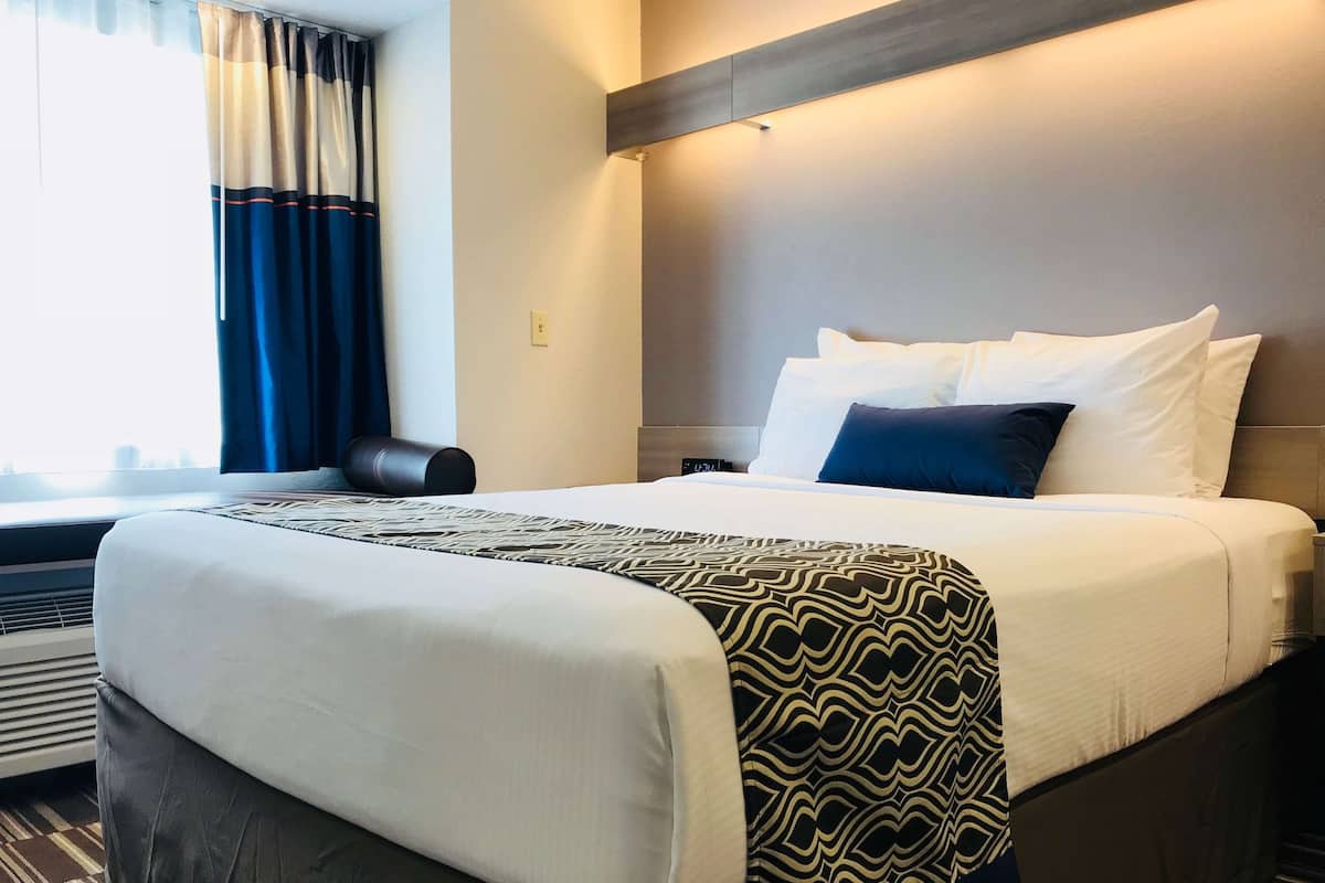 A neatly made bed with white and patterned bedding, a headboard, and a window with curtains.